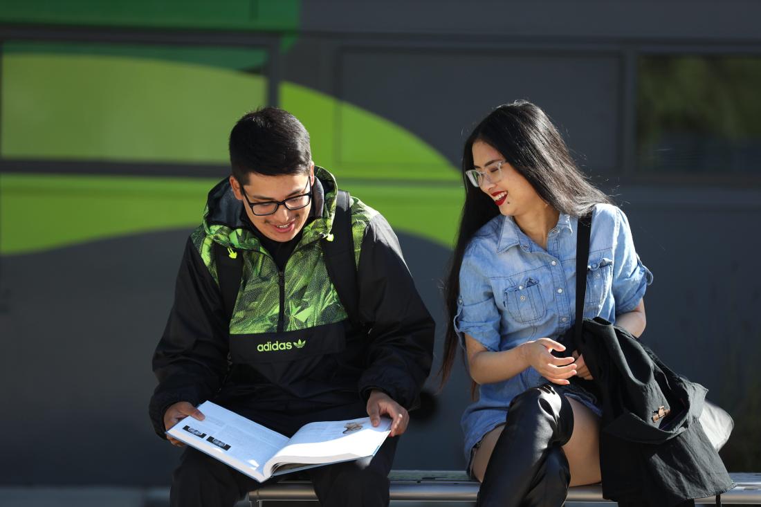 two students looking at a book outside