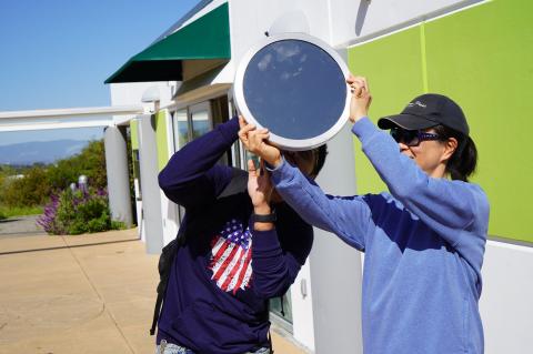 two people looking up at the sky during the day holding a reflector 